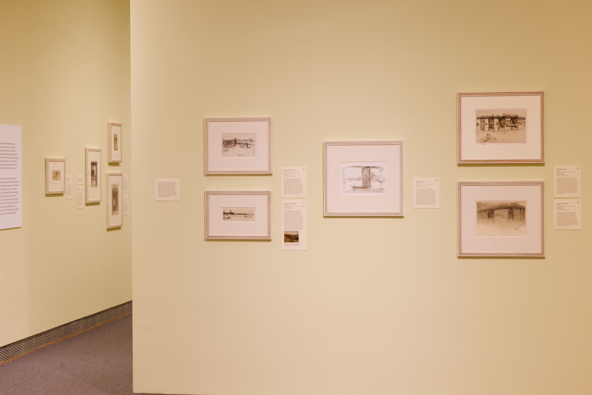 Framed etchings arranged on a pale yellow wall, accompanied by interpretive texts.