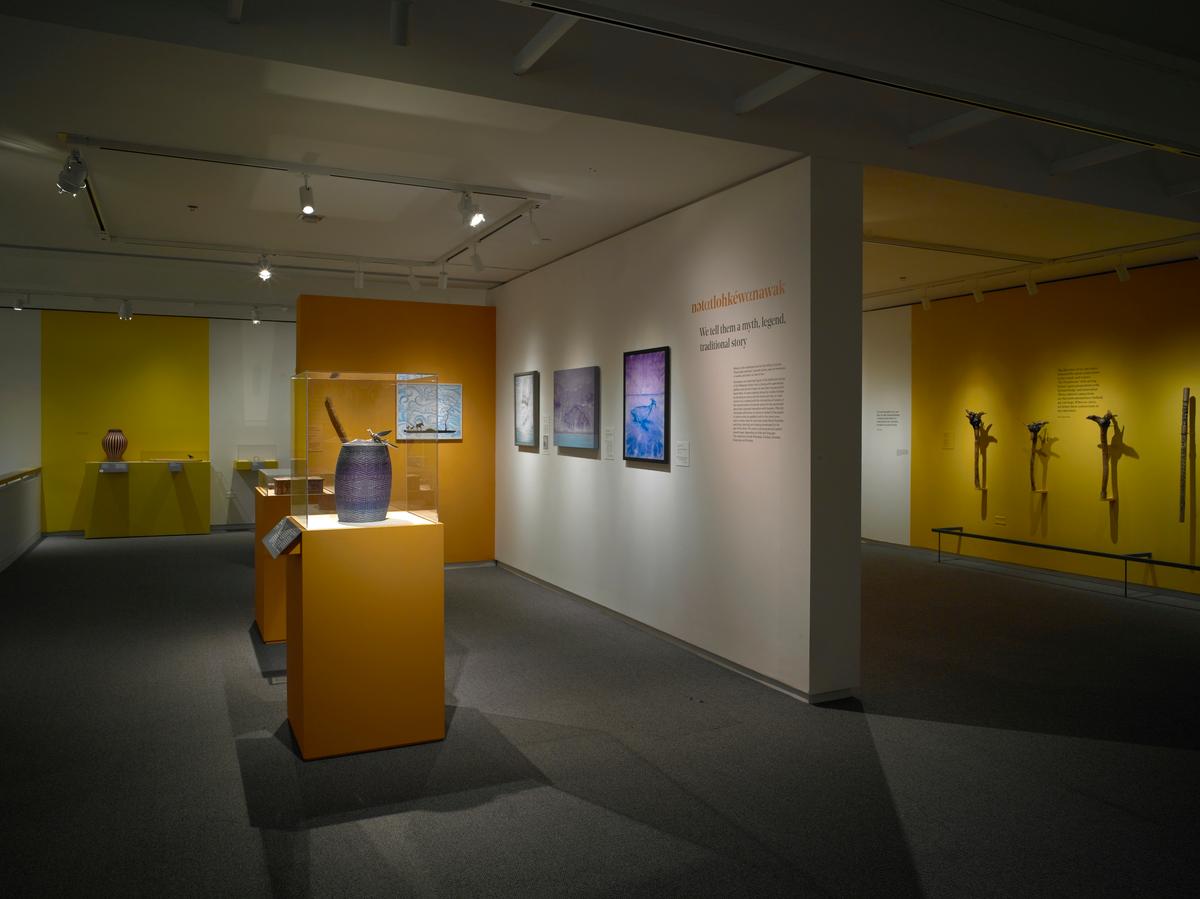 Ceramic vessels on yellow pedestals and framed artworks on white gallery walls with interpretive text