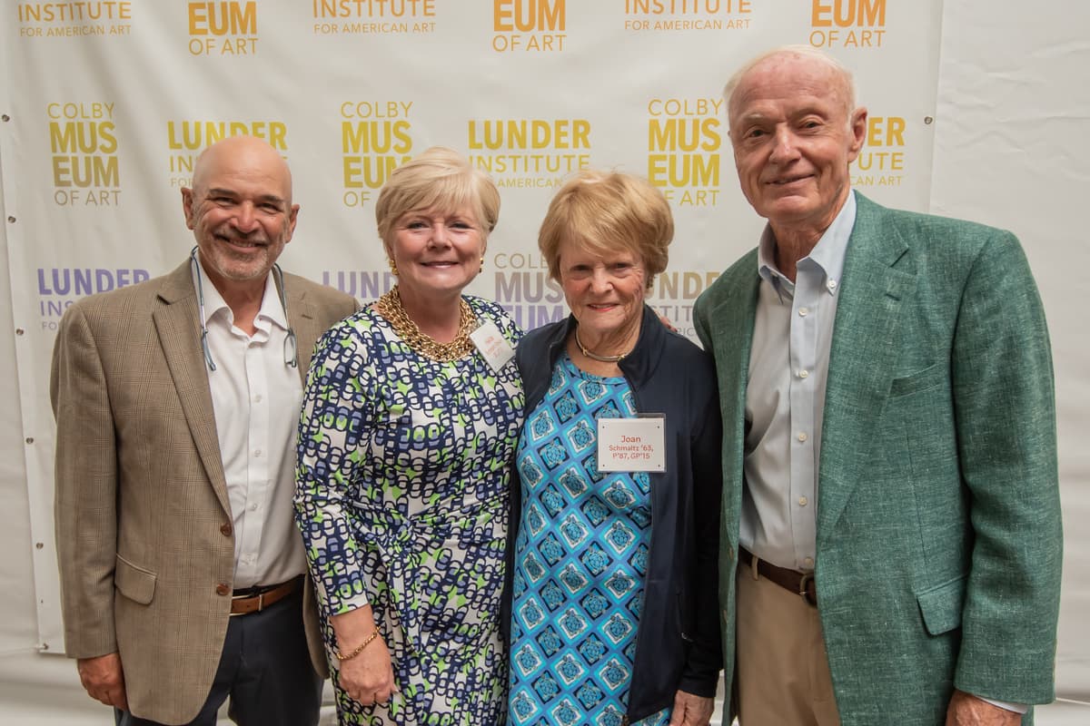Four individuals, including Heidi Schmaltz Dolan, Dick Schmaltz, Joan Dignam, Schmaltz posed for a picture in front of a wall with multi-colored Colby Museum of Art and Lunder Institute for American Art logos.
