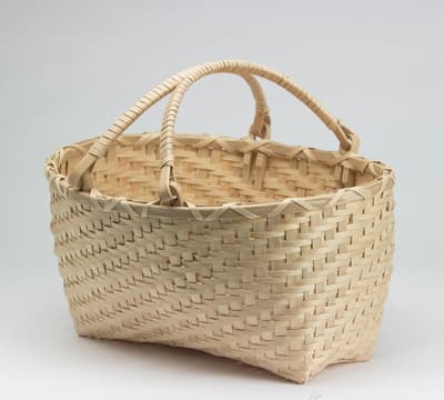 A woven shopping basket photographed in front of a plan gray background.