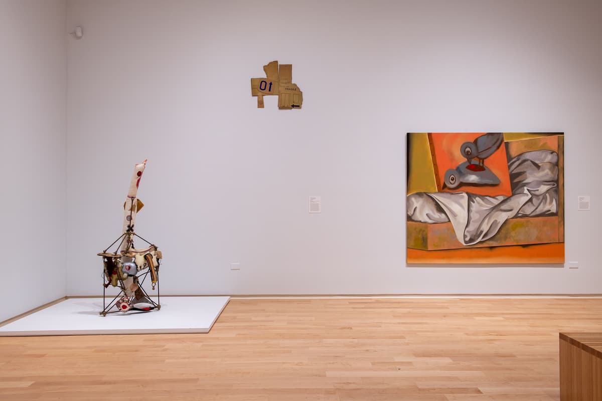 A white gallery wall featuring three small framed works on paper. To the right, a large circular wall sculpture made of concentric rings of neutral-toned fabric.