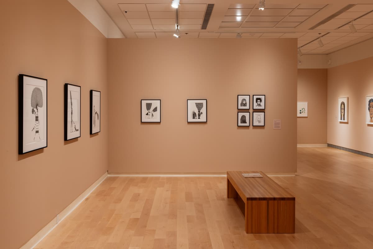 Framed black and white figurative drawings installed on multiple walls in a gallery.