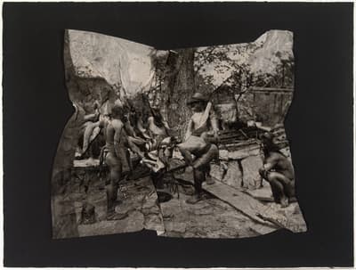 A black-and-white photograph that has been physically crumpled and then flattened, creating a fractured, mosaic-like effect. It depicts a group of Indigenous people in a forested setting. The photograph is mounted on a solid black rectangular background, emphasizing its distorted and weathered texture.