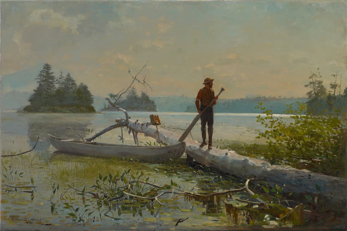 An oil painting of a lone woodsman standing on a large, fallen white birch log at the edge of a calm lake. The man, seen in profile facing right, wears a brown hat, vest, and trousers and holds a long wooden paddle. To his left, a gray canoe is tucked against the fallen log among lily pads and marsh grass. In the background, two small, pine-covered islands sit on the quiet water under a vast, hazy sky filled with soft, pale yellow and blue clouds. The light suggests early morning or late afternoon, casting a gentle glow across the scene. The signature "Winslow Homer 1870" is visible in the bottom left corner.