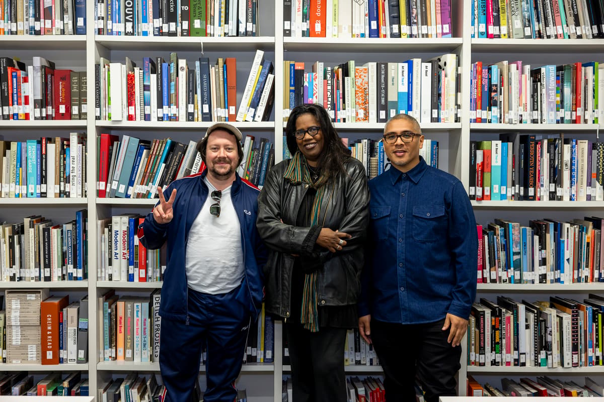 Three individuals standing in front a library shelf of books smile directly at a camera.