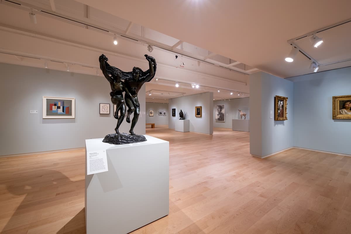 A wide-angle shot of the gallery centered on a bronze sculpture of two figures, with a mix of traditional portraits and modern abstract paintings on the surrounding walls.