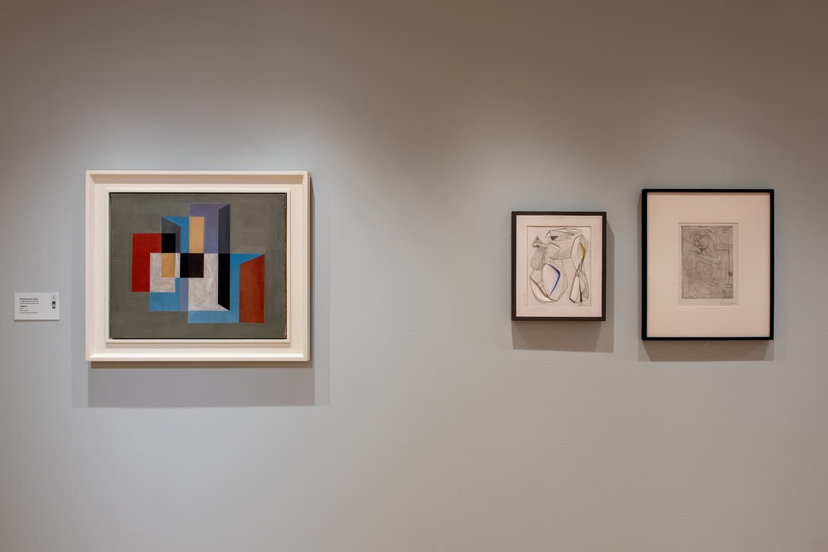 A close-up of three framed works on a gray wall: a colorful geometric abstract painting on the left, a small abstract sketch in the middle, and a delicate line drawing on the right.