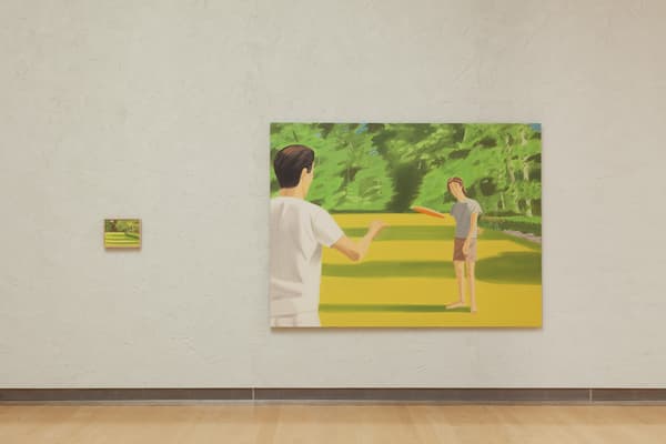 A straight-on view of a textured cream-colored wall showing two paintings. On the left is a very small, horizontally framed landscape painting. To its right is a large, horizontal painting depicting two figures playing frisbee on a vibrant yellow and green lawn, with a figure in a white shirt seen from behind in the foreground throwing a orange disc toward a figure standing in the distance.