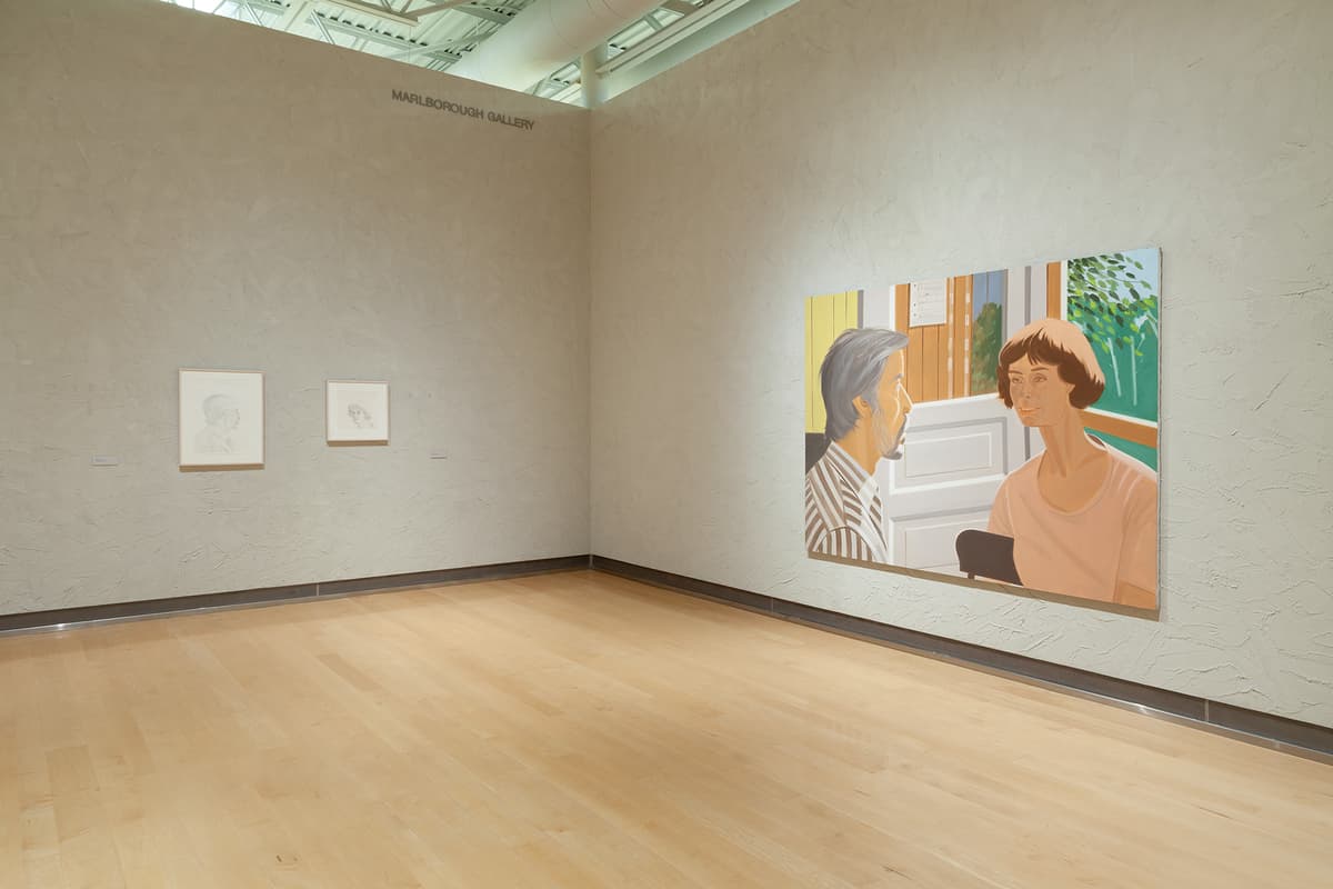 A corner view of a gallery space with a light wood floor. The wall on the left, under the text "MARLBOROUGH GALLERY," features two small, white-framed vertical portrait drawings. The wall on the right features a large, colorful horizontal painting of a man with gray hair in a striped shirt and a woman with brown hair in a pink shirt facing each other indoors, with green trees visible through a window behind them.