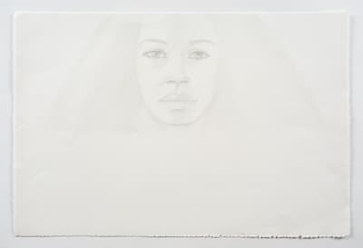 A faint, centered pencil drawing of a woman's face on a large sheet of white paper . The portrait features large, detailed eyes and a neutral expression, with very light shading indicating long, voluminous hair.