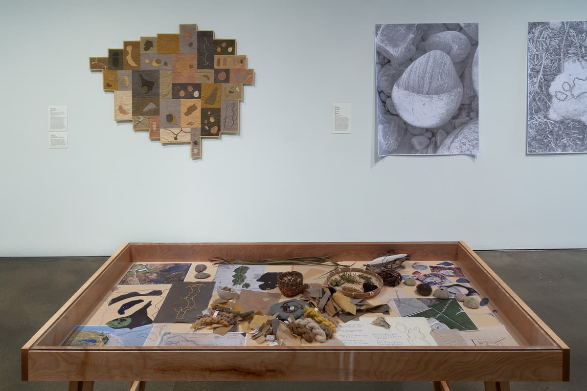An installation view of a white gallery wall showcasing five large, loosely handled portrait sketches in matching light wood frames. The sketches depict various faces and expressive figures drawn in dark charcoal or ink on light-colored paper. The artwork arrangement hangs uniformly above a reflective, light-colored hardwood floor.