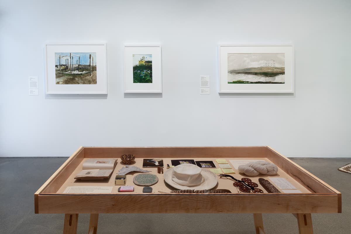 An installation view of a gallery corner featuring bright coral-pink walls and light hardwood flooring under track lighting. The left wall displays four small, white-framed drawings of flowers arranged horizontally. The back wall features a large salon-style grid arrangement of eighteen small white-framed minimalist line drawings.