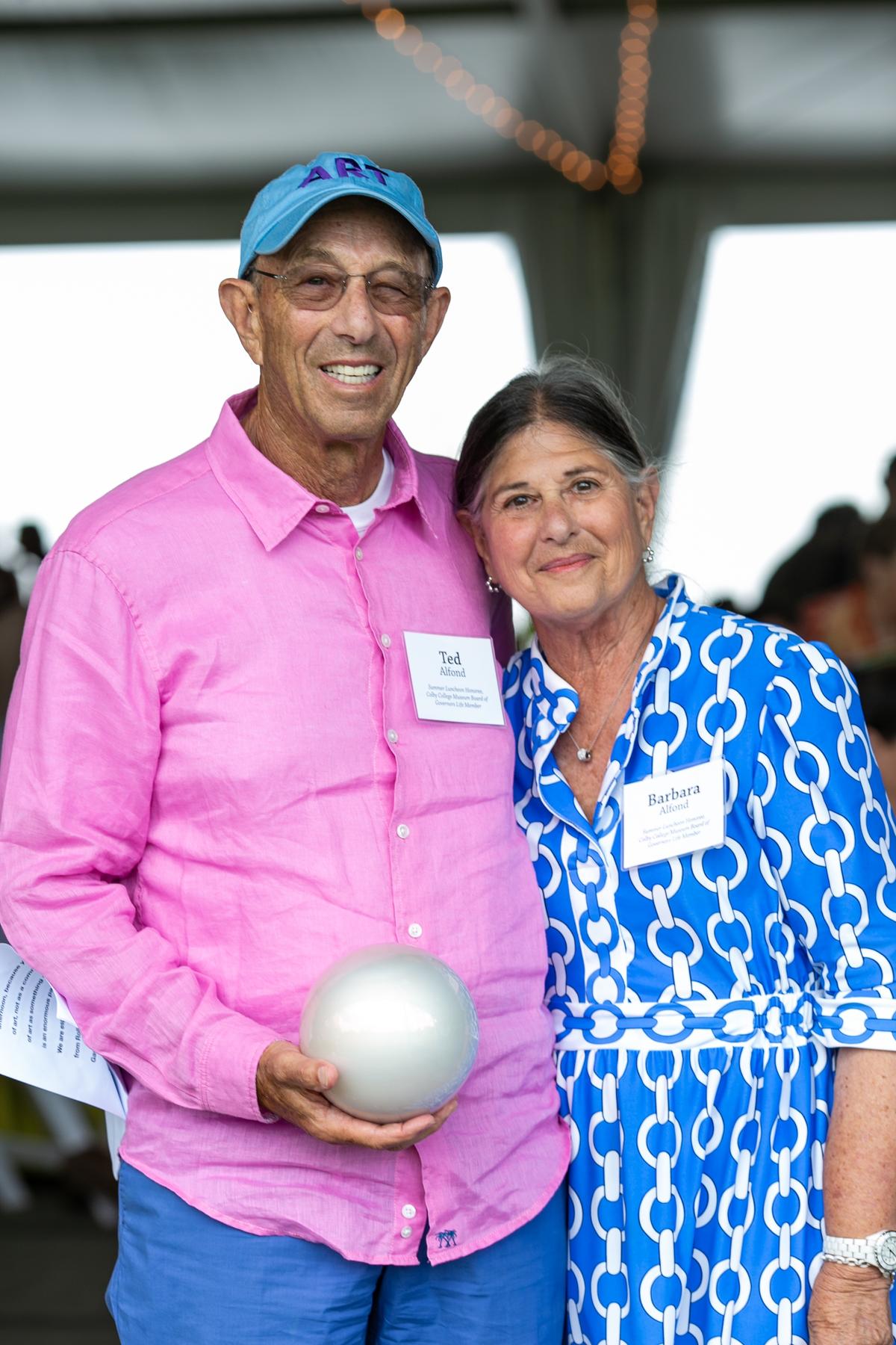 Two people smile for the camera at the Summer Luncheon. The person on the left holds a white circular object.