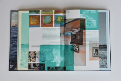 An open multi-page catalog displaying a highly layered collage spread on a light-grey background. The layout features columns of printed text overlaid with semi-transparent geometric color blocks in teal, orange, and grey. Scattered across the pages are several small images: food preparation photos in the bottom left, an architectural window detail in the center, and a tiny framed portrait on the far right. Glimpses of a blue sea landscape on the book's endpaper are visible on the left.