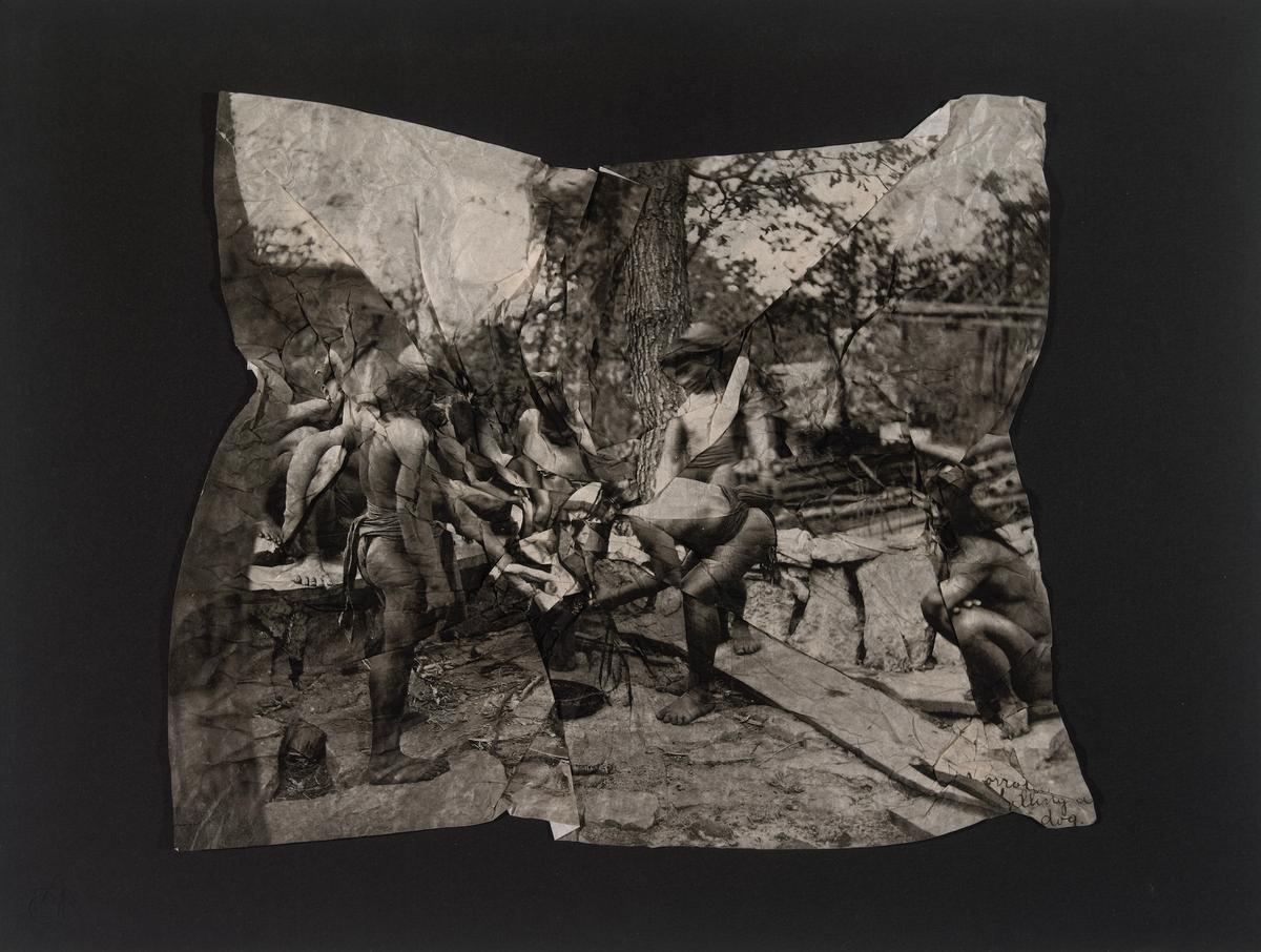A sepia-toned, black-and-white photo-collage or altered print presented on a solid dark background. The central image is a crinkled, distorted, and fragmented photograph depicting several figures—seemingly indigenous individuals wearing loincloths—outdoors in a wooded setting. One figure stands on the left in profile, while another crouches or bends near the center alongside a wooden plank, and a third figure is crouched on the far right. Faint handwritten script text is visible in the bottom right corner of the crumpled paper.