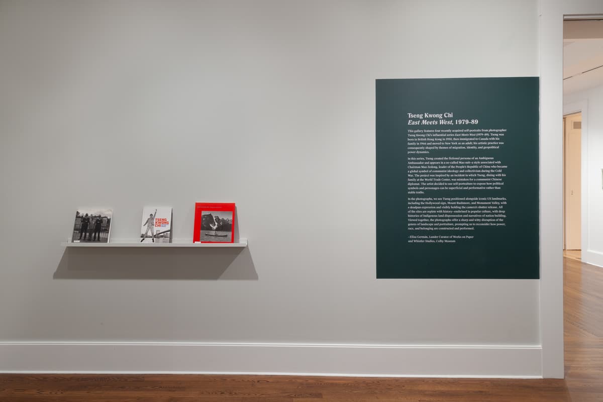 A grey gallery wall. On the left, a floating bookshelf with three art publications and on the right, a dark green rectangle with white text. The heading reads "Tseng Kwong Chi East Meets West, 1979-89.