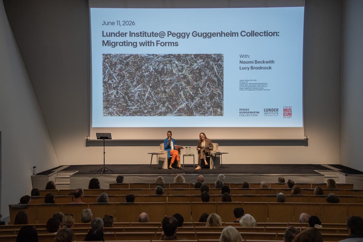 Two speakers sit on stage in an auditorium beneath a large projection screen for a talk titled "Lunder Institute @ Peggy Guggenheim Collection: Migrating with Forms," featuring Naomi Beckwith and Lucy Bradnock. An audience is seated in the foreground.