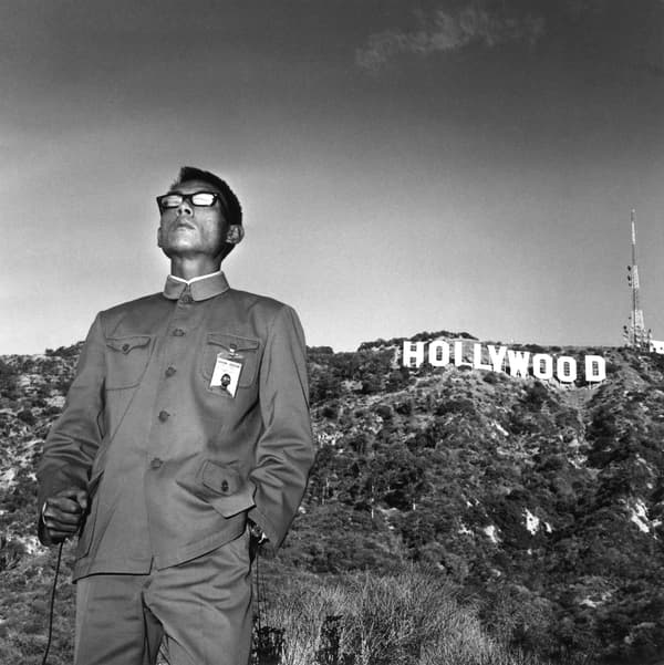 Black and white portrait of Tseng Kwong Chi standing in front of the Hollywood sign.