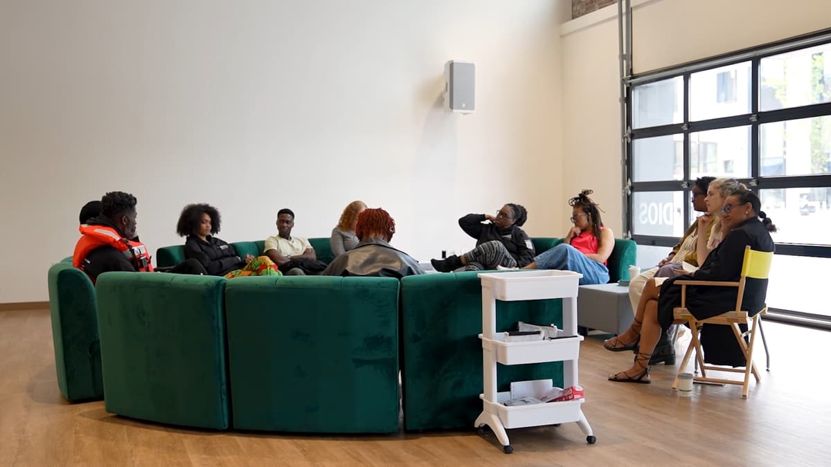 A group of people seated in a circle on a green velvet sofa and folding chairs