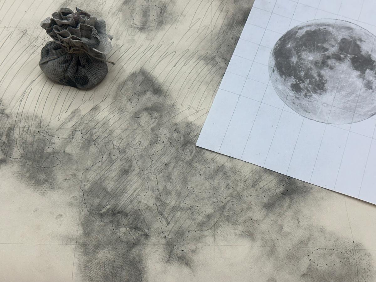 Image of a moon on paper and material used for spolvero on a surface covered in dark pigment.