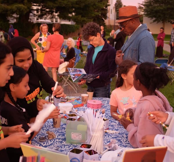 Children and adults gathered around a table with books and art-making supplies.