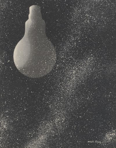 Black-and-white photogram print depicting a translucent silhouette of an inverted lightbulb on the left. The bulb hovers over a dark background filled with a dense, diagonal swath of white stippling and specks resembling a night sky or galaxy. Signed "Man Ray" in the lower right of the image.