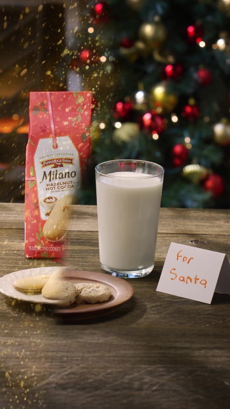 Glass of milk and a plate of cookies on a wooden table with a note for Santa, decorated Christmas tree lit behind