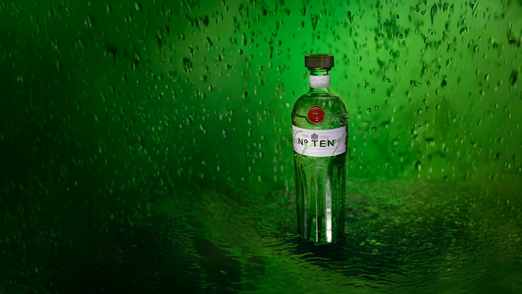 Tanqueray No. Ten bottle standing in shallow water against a deep green wall of falling droplets