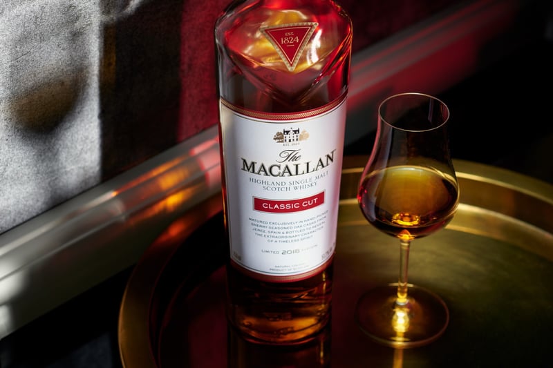 A Macallan bottle beside a filled nosing glass on a reflective surface under warm light