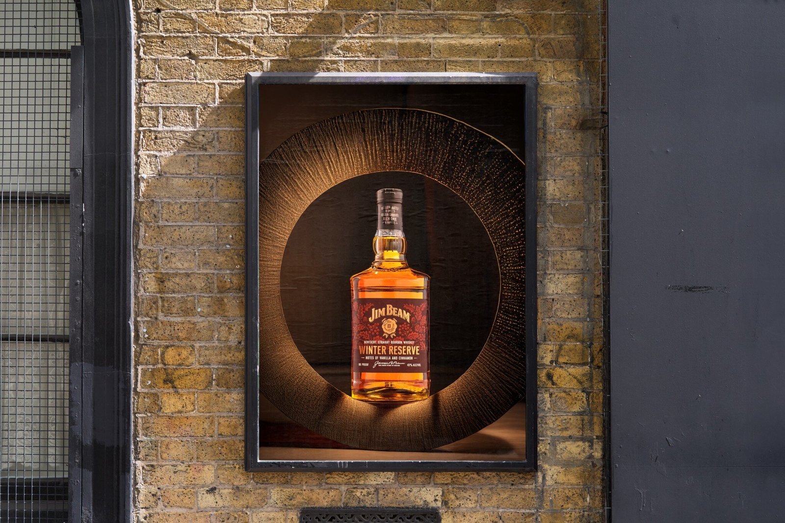 Jim Beam Winter Reserve bottle in a lit alcove set into an old brick wall, dark doorway to one side