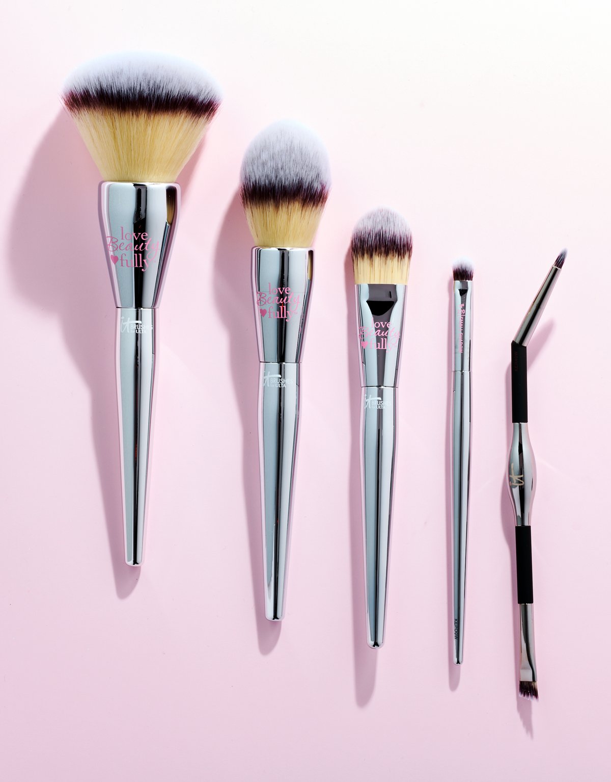 Five makeup brushes fanned in descending size across a pale pink ground