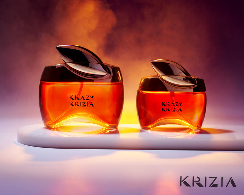 Two amber Krizia fragrance bottles lit from below against a smoky peach backdrop