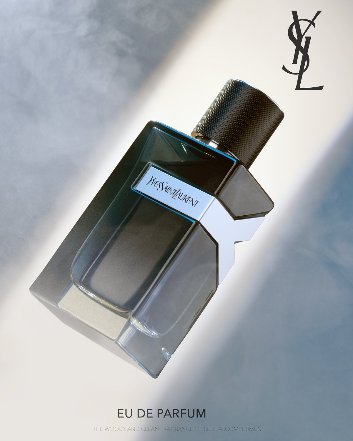 A dark Yves Saint Laurent eau de parfum bottle lying on a pale grey surface in raking light