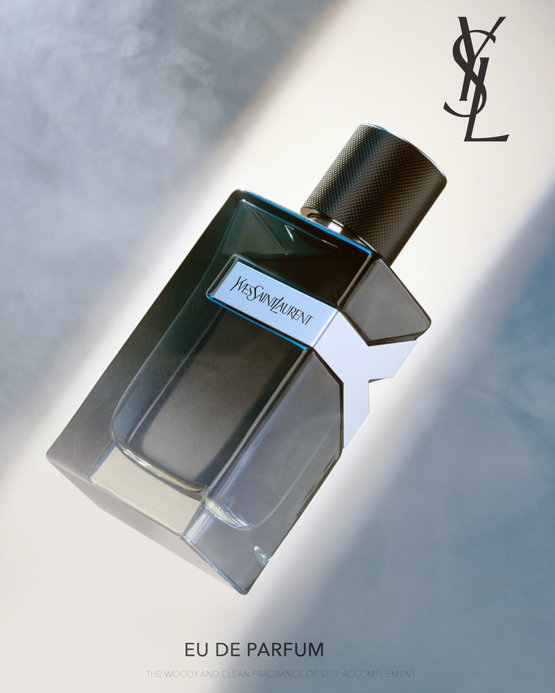A dark Yves Saint Laurent eau de parfum bottle lying on a pale grey surface in raking light