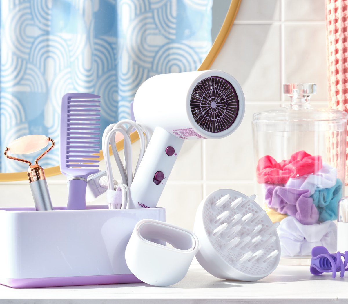 A lilac hair dryer, comb and grooming tools arranged on a pale pastel bathroom set with folded towels