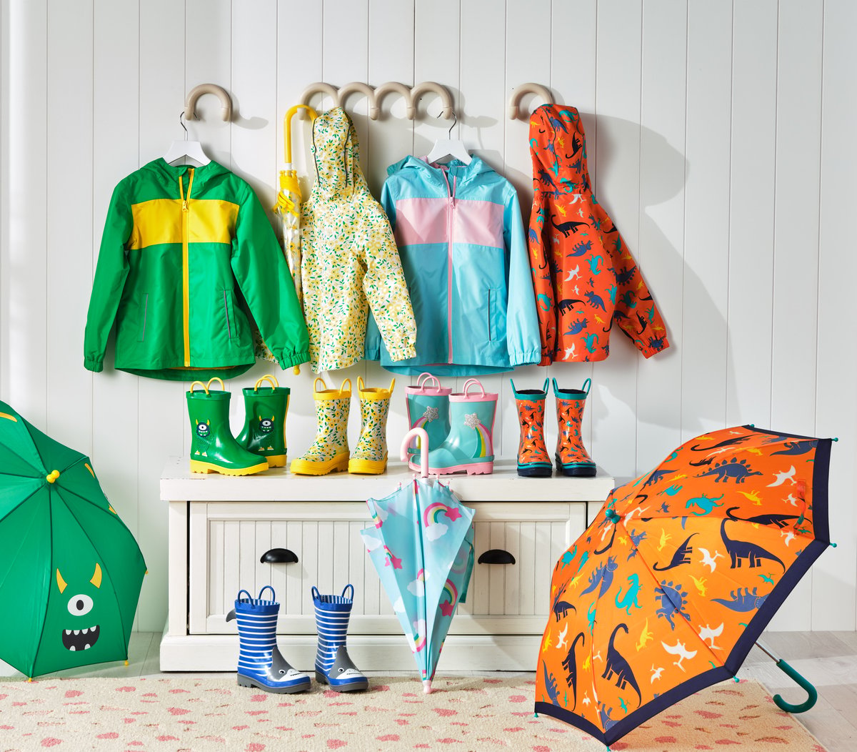 Children's rainwear hung on a white rack with wellington boots and open umbrellas below