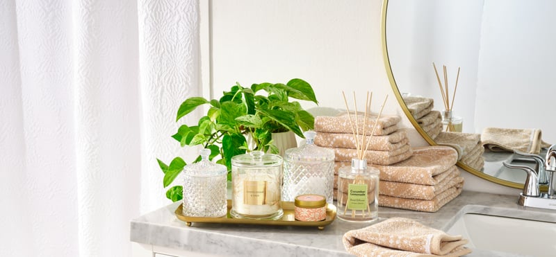 A bathroom counter styled with plants, reed diffusers, rolled towels and candles