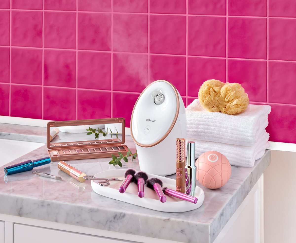 Makeup and a lit vanity mirror arranged on a marble counter against a hot pink tiled wall