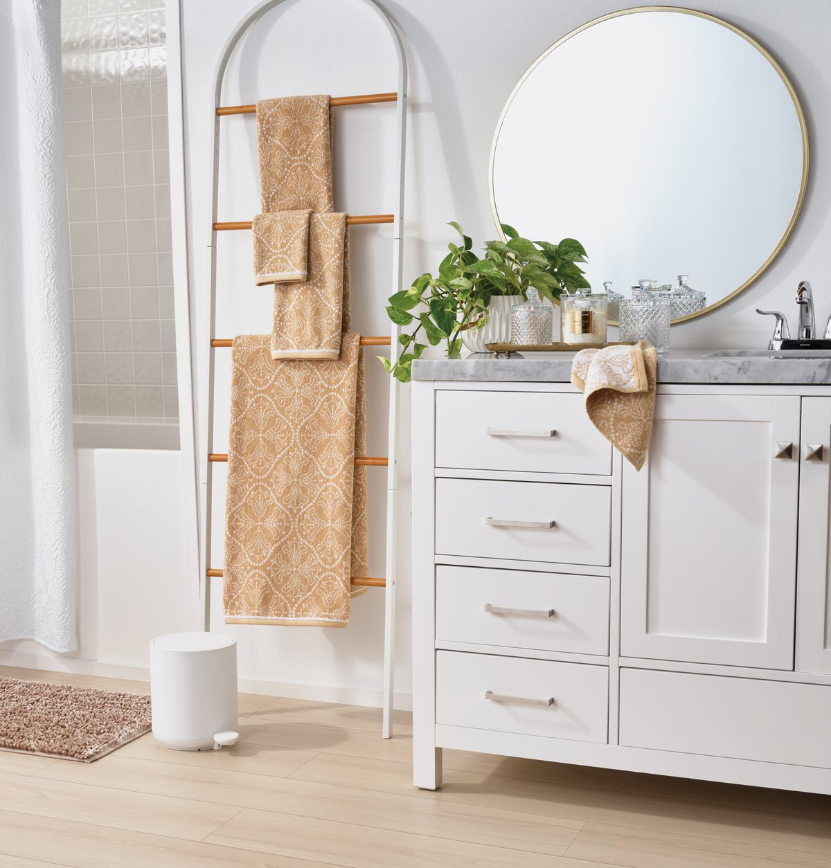 A white bathroom with folded towels on a ladder rail, a round mirror and a plant on the vanity