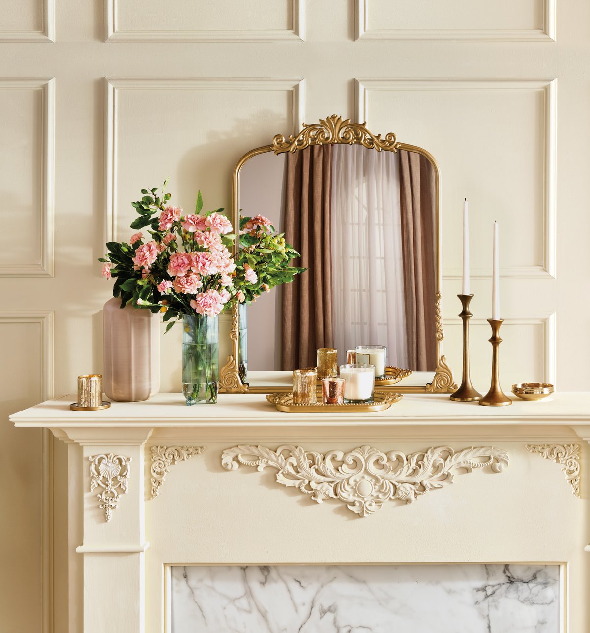 Styled mantelpiece with a gilt mirror, pink hydrangeas, brass candlesticks and a marble surround in soft daylight