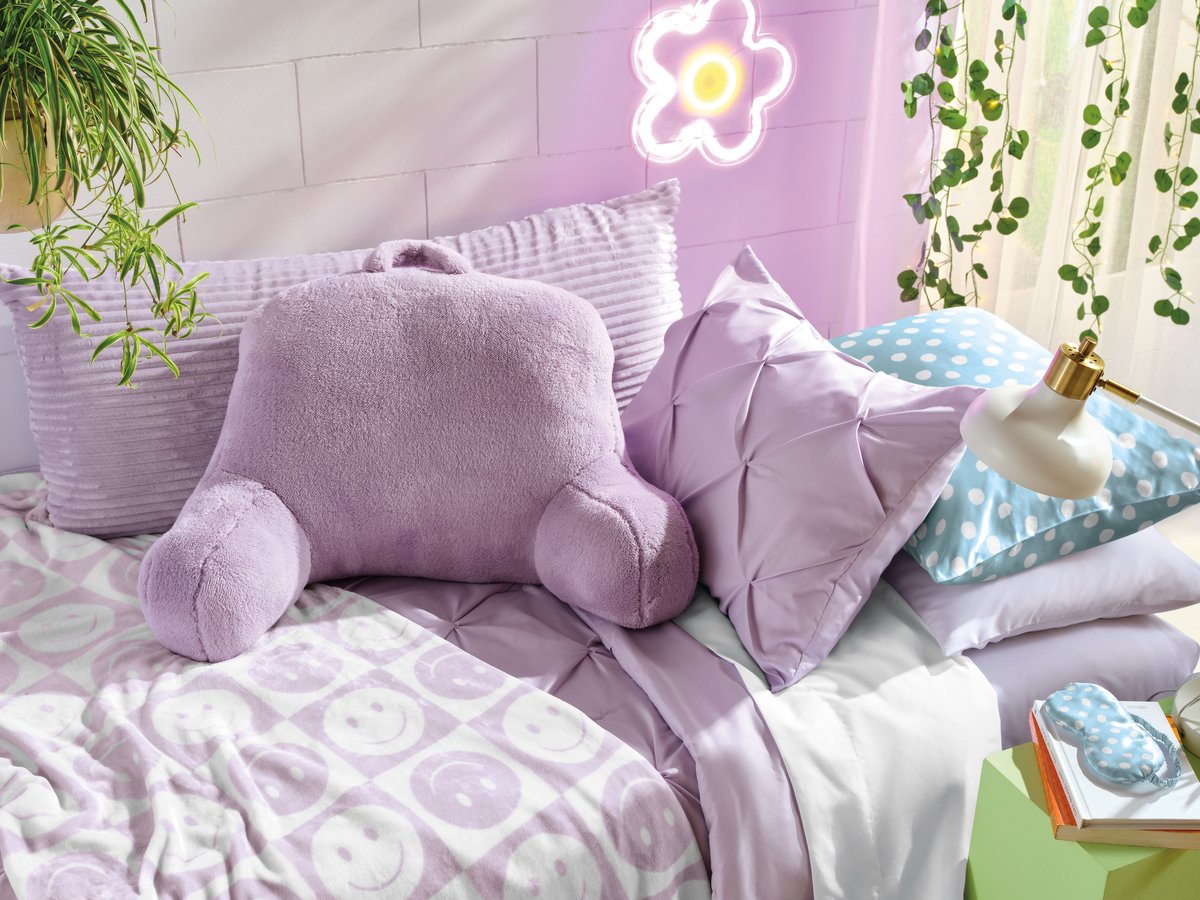 A lilac bedroom styled with a plush cushion, floral wall decal and trailing plants