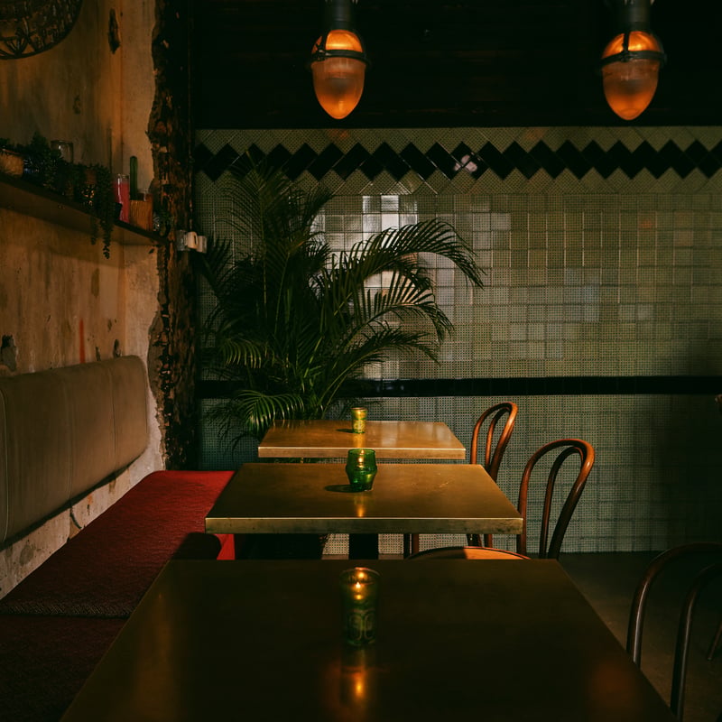 A dim restaurant with green tiled walls, bentwood chairs and glowing pendant lamps