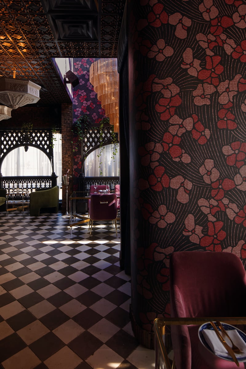 Ornate hotel interior — checkerboard marble floor, patterned crimson wallpaper, arched openings and pressed tin ceiling