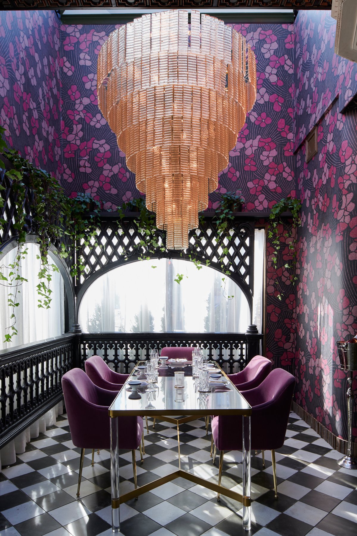A dining nook with a crystal chandelier, floral wallpaper and purple velvet chairs on a chequered floor