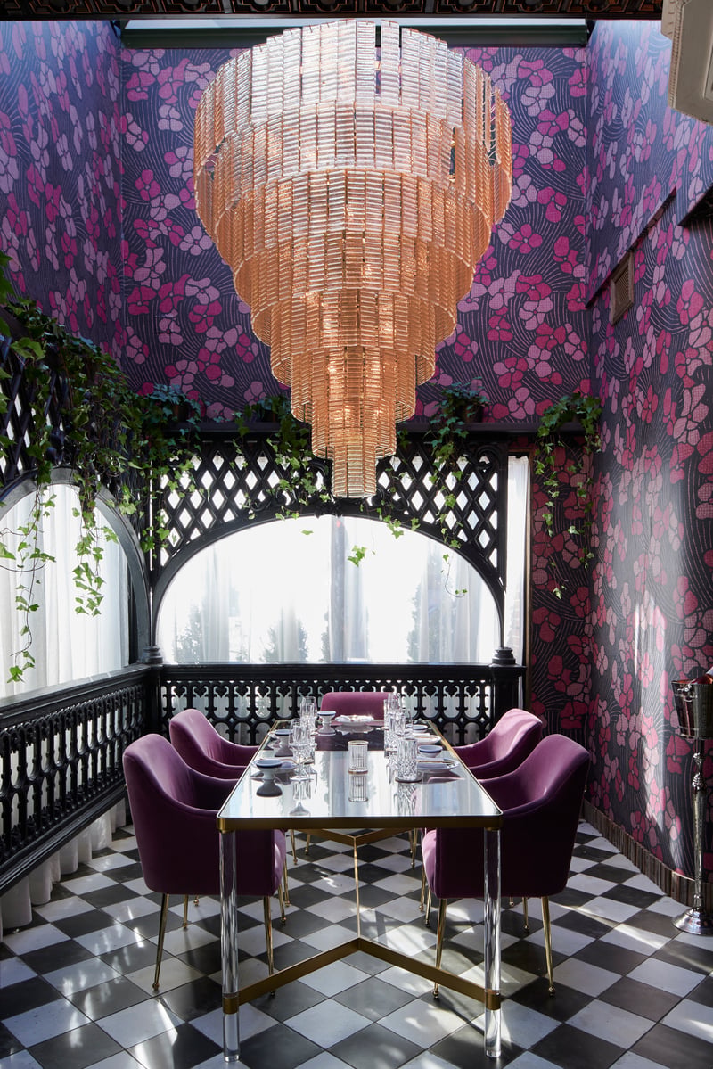 A dining nook with a crystal chandelier, floral wallpaper and purple velvet chairs on a chequered floor