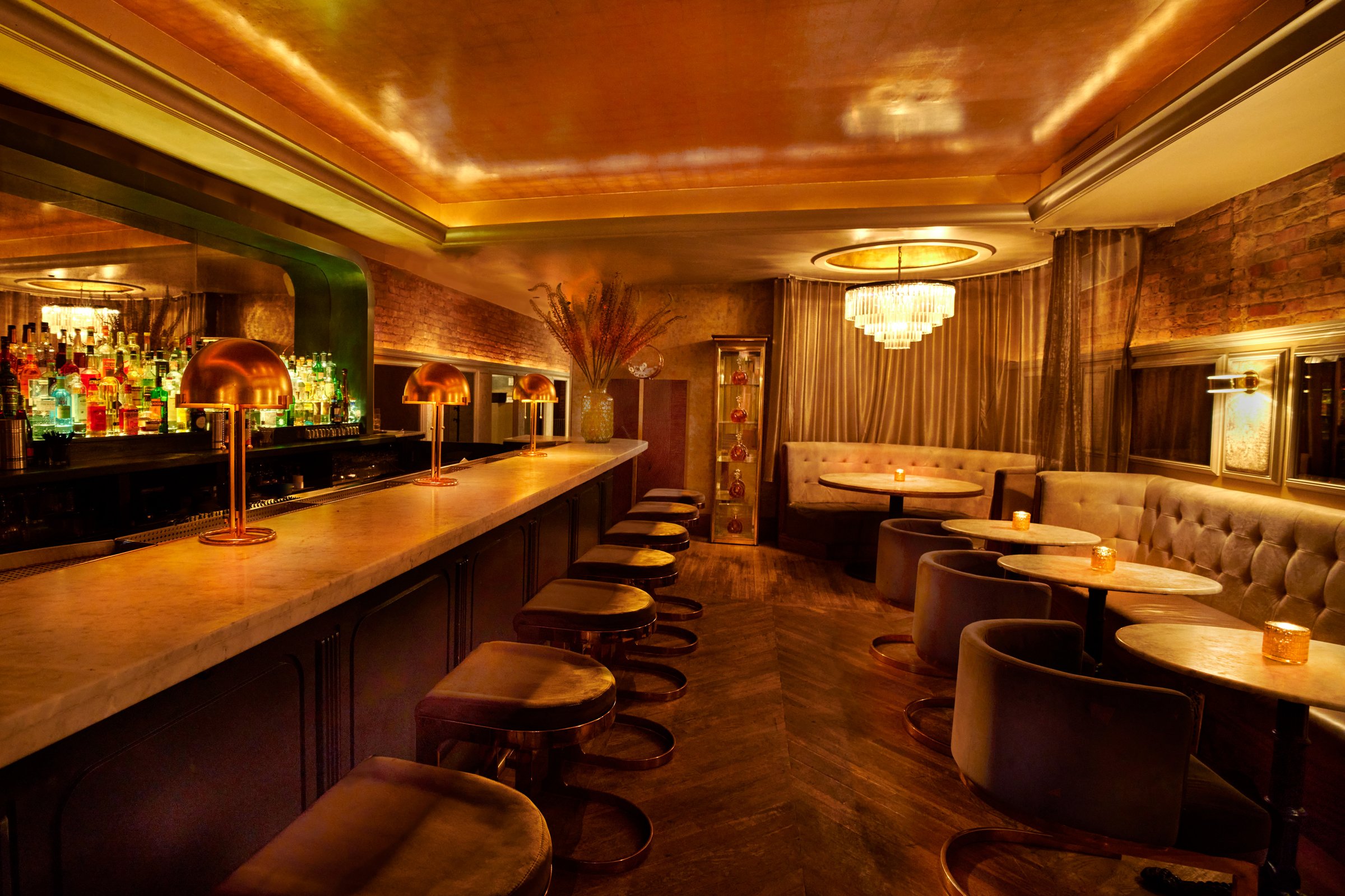 A long warm-lit bar with upholstered stools running the length of a panelled room