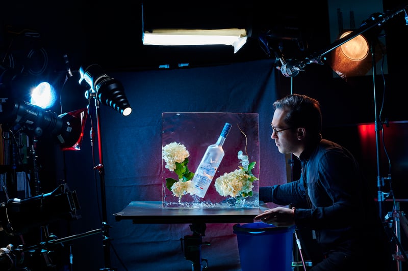 A photographer at work on a lit set, a Grey Goose bottle and flowers arranged on the table