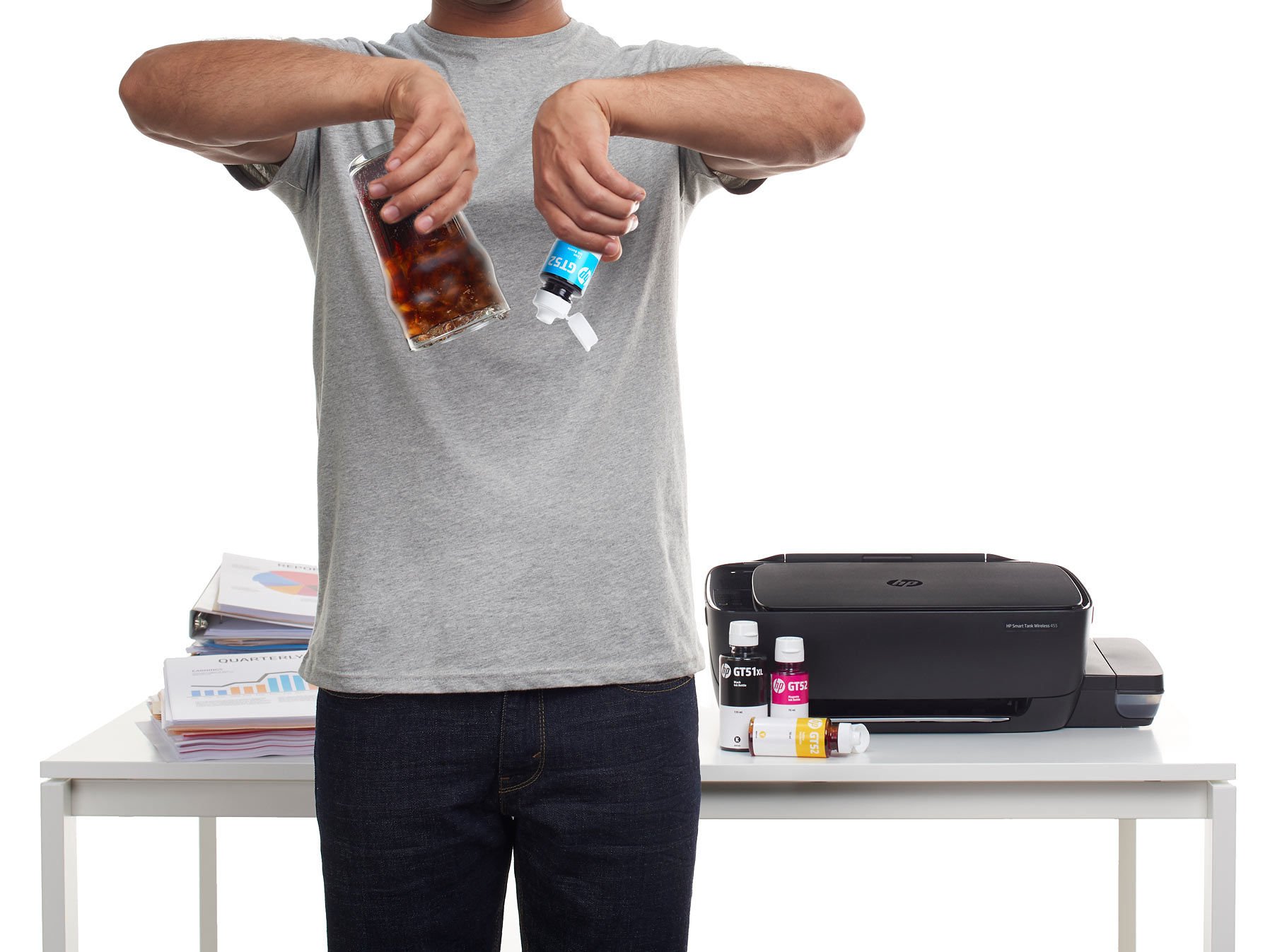 A man in a grey t-shirt tears a printed sheet in half beside a printer on a white table