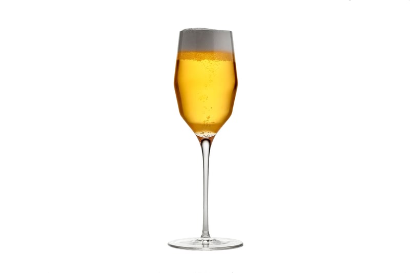A stemmed glass of pale golden beer with a white head, photographed on white