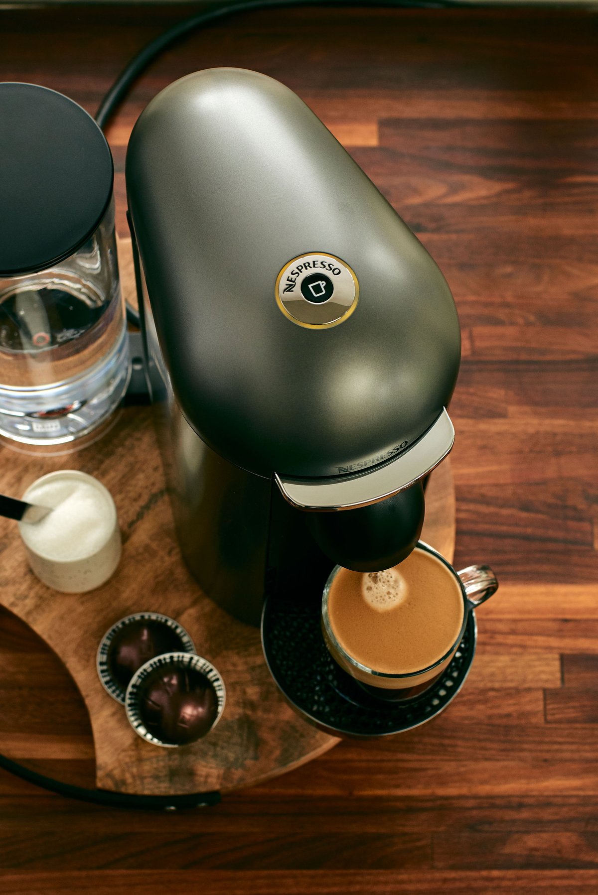 A dark green Nespresso machine on a wooden counter with a filled cup and capsules